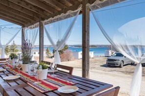An outdoor dining area with a wooden table set for a meal, overlooking a body of water and a parked car. - Spyglass Seasted | Stunning Ocean Views & Coastal Comfort (Chester Basin)
