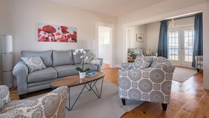 A modern living room with a grey sofa, patterned armchairs, a wooden coffee table, and a large window with curtains.