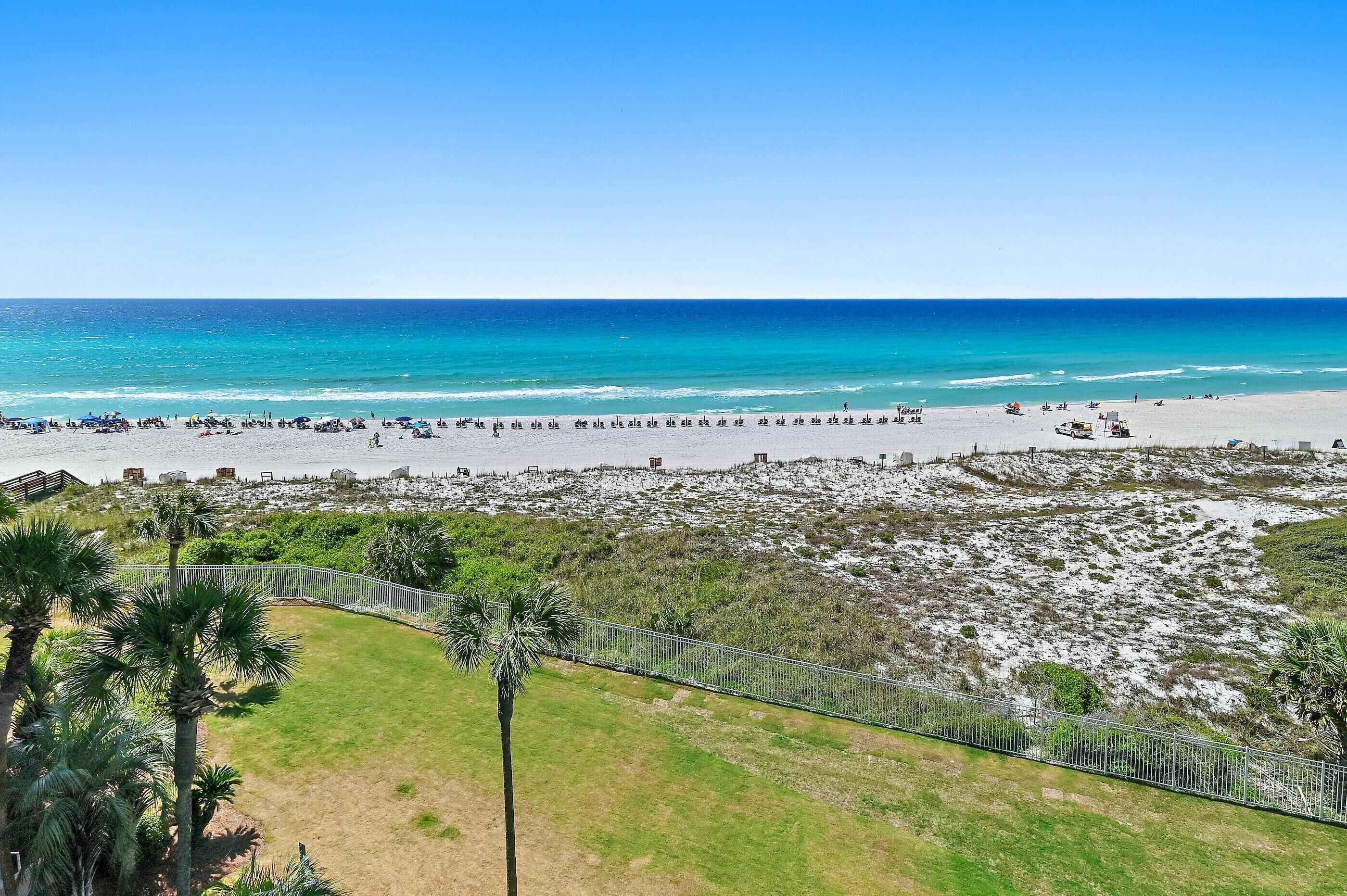 A beach with a fenced area, palm trees, and a clear view of the ocean.