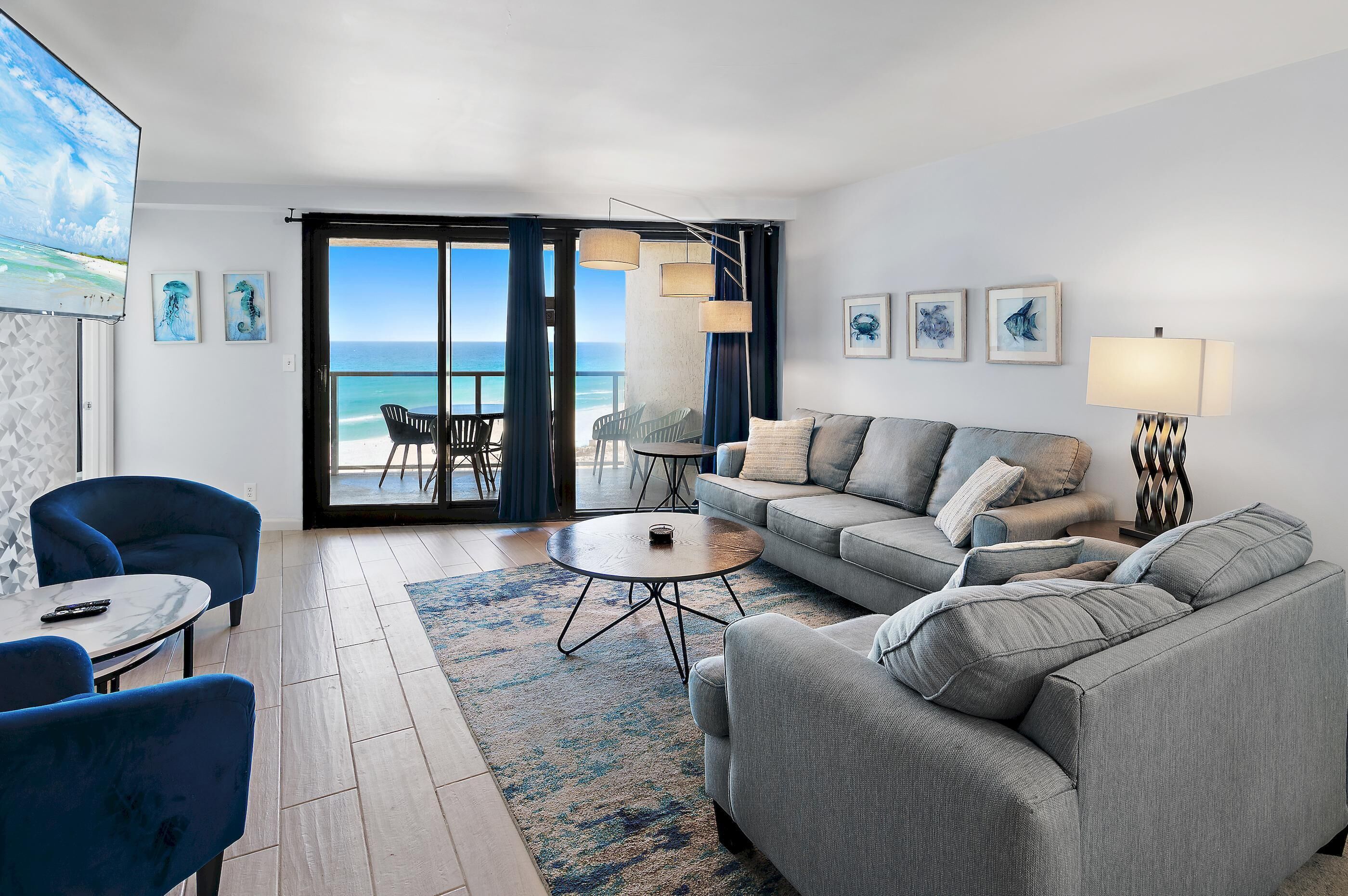 Ein modernes Wohnzimmer mit einer Couch, Sesseln, einem Couchtisch und Blick auf den Ozean durch große Glasfenster.