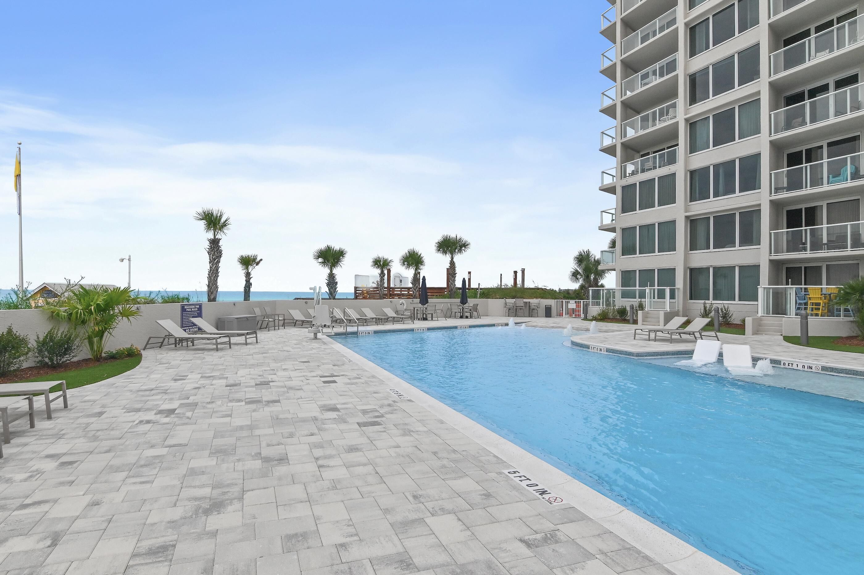 A swimming pool with lounge chairs, palm trees, and a multi-story building.
