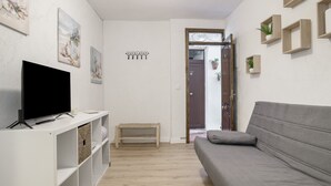 A living room with a flat-screen TV, a grey sofa, a small bench, and wall-mounted shelves. - Apartment ‘Vacacional En Vejer’ (Vejer de la Frontera)