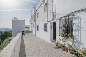 A narrow cobblestone street with a white building, potted plants, and a motorcycle parked on the side. - Apartment ‘Vacacional En Vejer’ (Vejer de la Frontera)