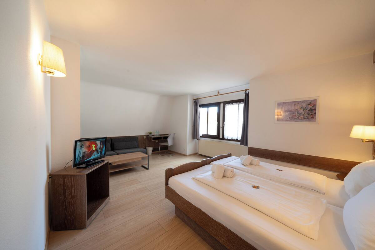 A hotel room with a bed, a desk, a television, and a window with curtains.