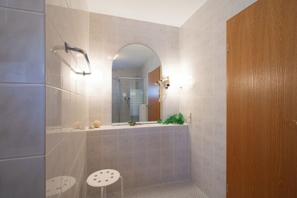 Une salle de bain avec une douche, des toilettes, un petit tabouret, un miroir et une porte en bois.