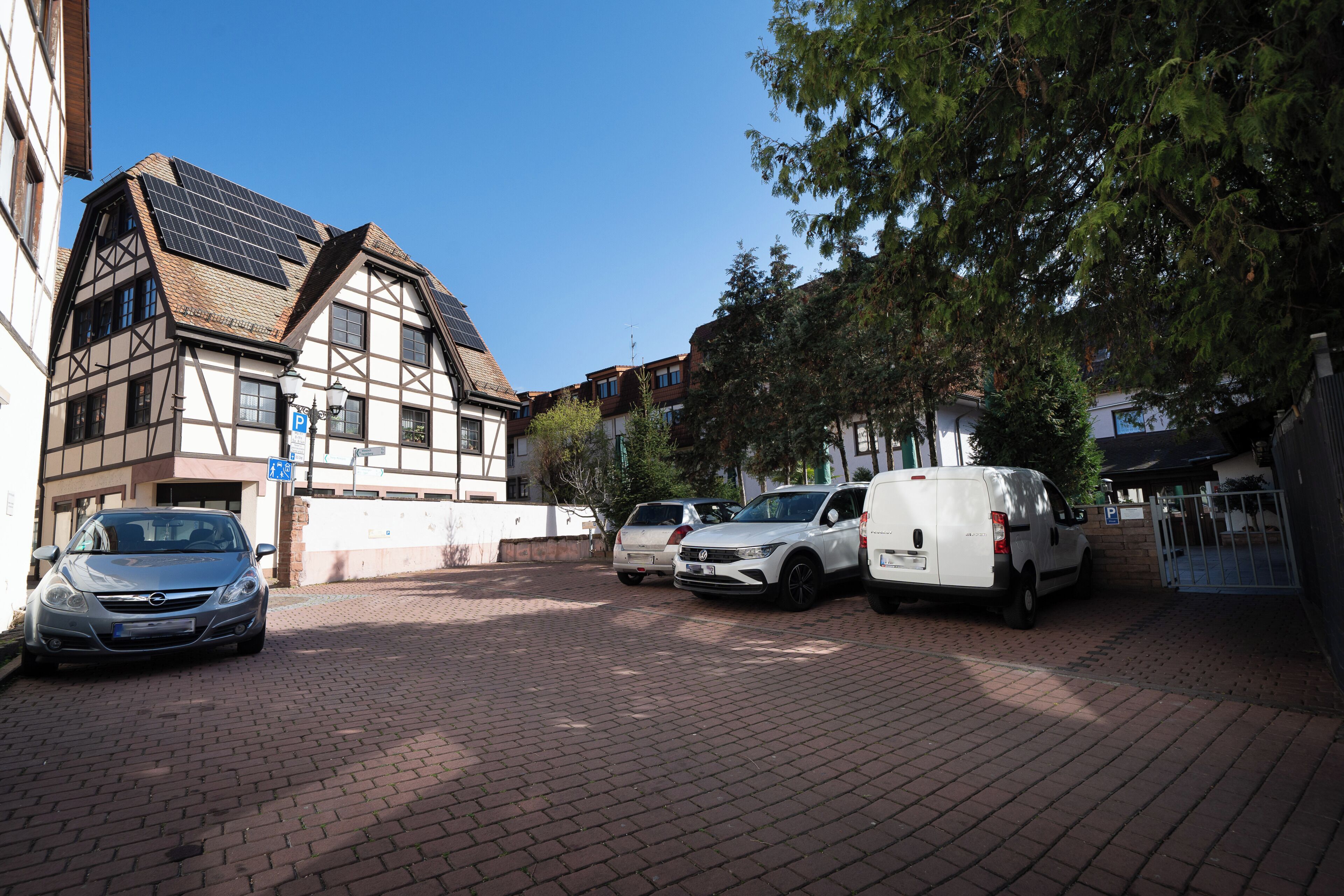 A parking area with cars, a building with solar panels, and a tree.