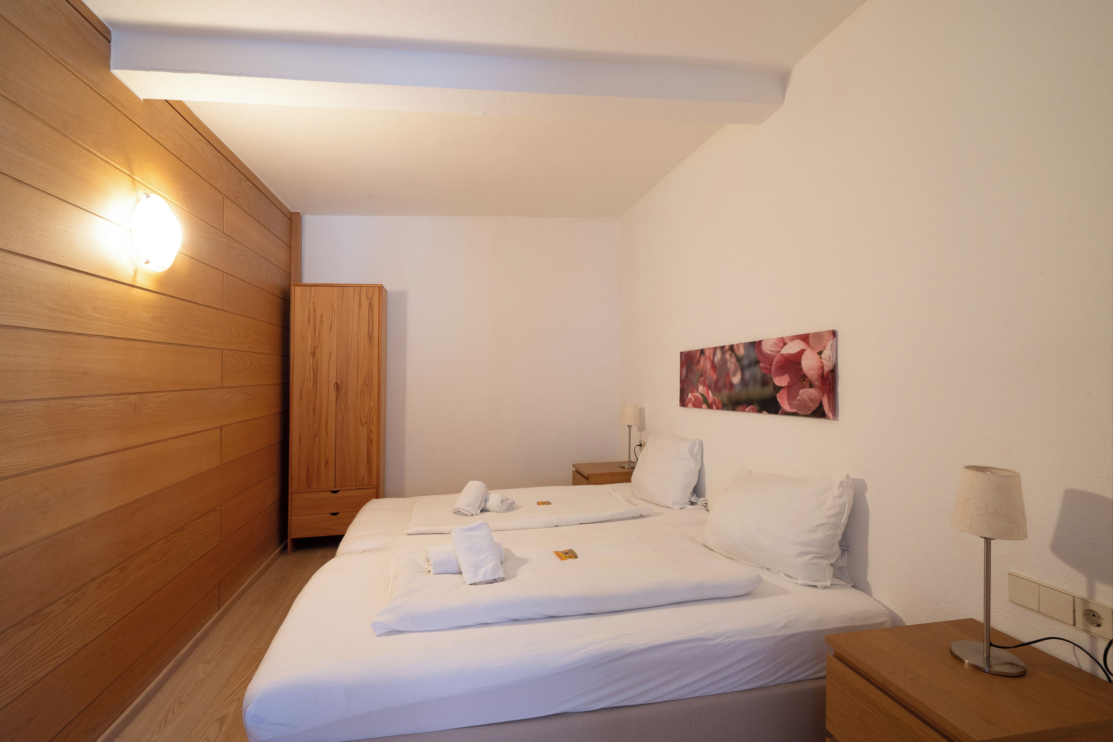 Une chambre d’hôtel avec des murs lambrissés, un lit recouvert de draps blancs, une table de chevet avec une lampe et un tableau accroché au mur.