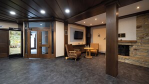 A room with a stone fireplace, a television mounted on the wall, a seating area with a table and chairs, and a refrigerator stocked with beverages. - Hotel Bären (Leimen)