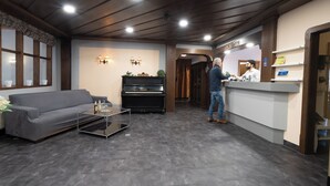 A reception area with a piano, a grey sofa, and a reception desk. - Hotel Bären (Leimen)