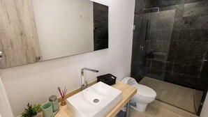 Een moderne badkamer met een witte wastafel, een spiegel, een toilet en een douche.