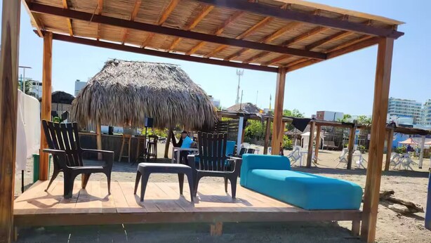 Een terras met overdekte zitplaatsen, een rieten dak, een houten pergola en blauwe kussens.