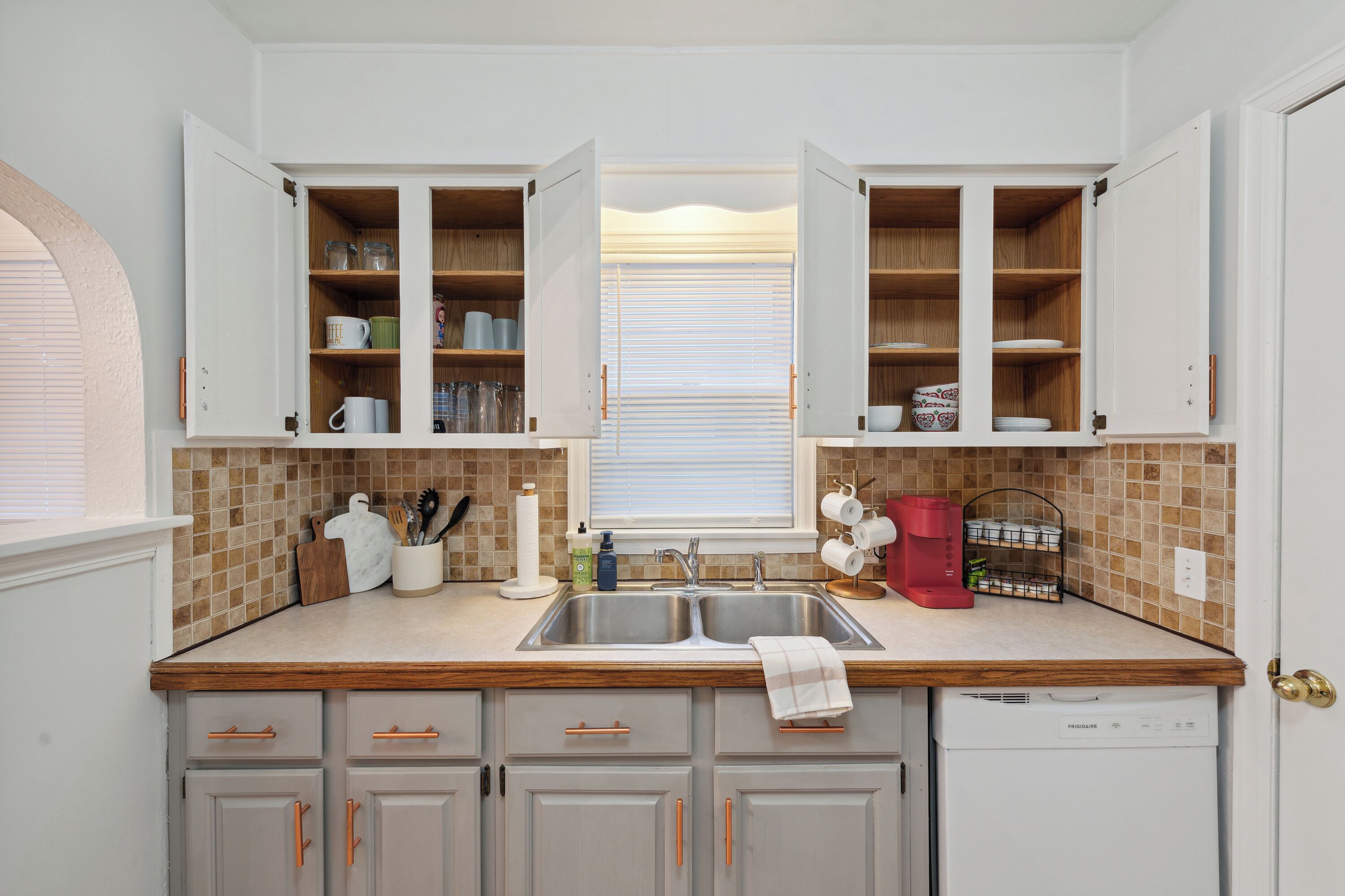 A kitchen with open cabinets, a double sink, and a dishwasher.