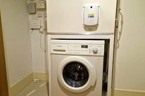 Eine kompakte, weiße Waschmaschine mit digitaler Bedienblende, in einem kleinen Waschraum mit schlichter Wand und Tür.