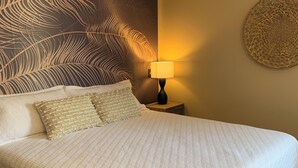 A neatly made bed with a white quilt, a wall mural of palm leaves, a round woven wall art piece, and a bedside lamp. - Private Pool Oasis Less Than 2 Miles to PC Beach! (Panama City Beach)