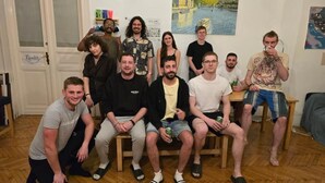 A group of people in a room with wooden flooring, a door labeled "Patrinho", and a painting of a castle on the wall. - Spicy Hostel (Budapest)