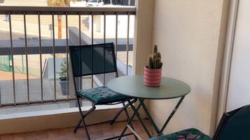 Un balcón con una mesa, sillas, una planta en maceta y vista a un edificio moderno.