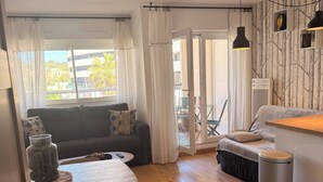 Un salon moderne avec un canapé, une table à manger et des chaises. On y trouve une poubelle et une fenêtre avec des rideaux.