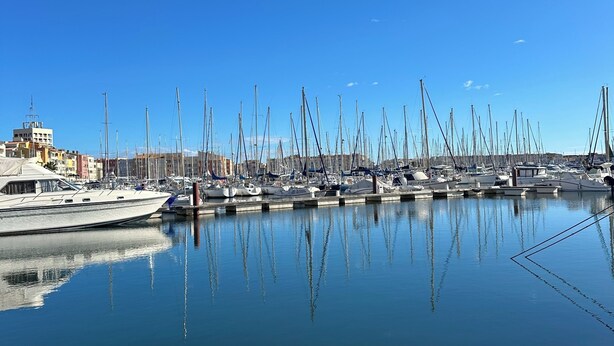 Un port de plaisance où sont amarrés de nombreux voiliers, avec une eau calme et un ciel bleu dégagé.