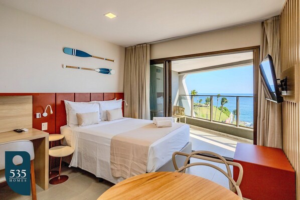 Ein Hotelzimmer mit Bett, Schreibtisch, Stuhl, Fernseher und einem Balkon mit Meerblick.