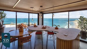 Une cuisine moderne dotée d’un grand îlot central, de grandes fenêtres offrant une vue sur l’océan et donnant sur la plage.