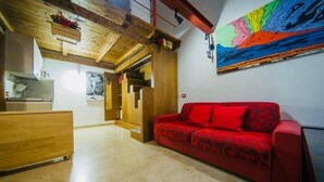 A modern interior with a wooden ceiling, a red sofa, and a colorful abstract painting. - Wonderful Holiday Home in the Historic Center of Naples in Piazza Bellini (Napoli)
