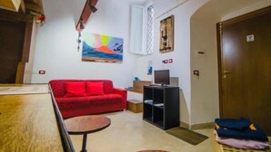 A room with a red sofa, a TV on a stand, a painting on the wall, and a wooden door. - Wonderful Holiday Home in the Historic Center of Naples in Piazza Bellini (Napoli)