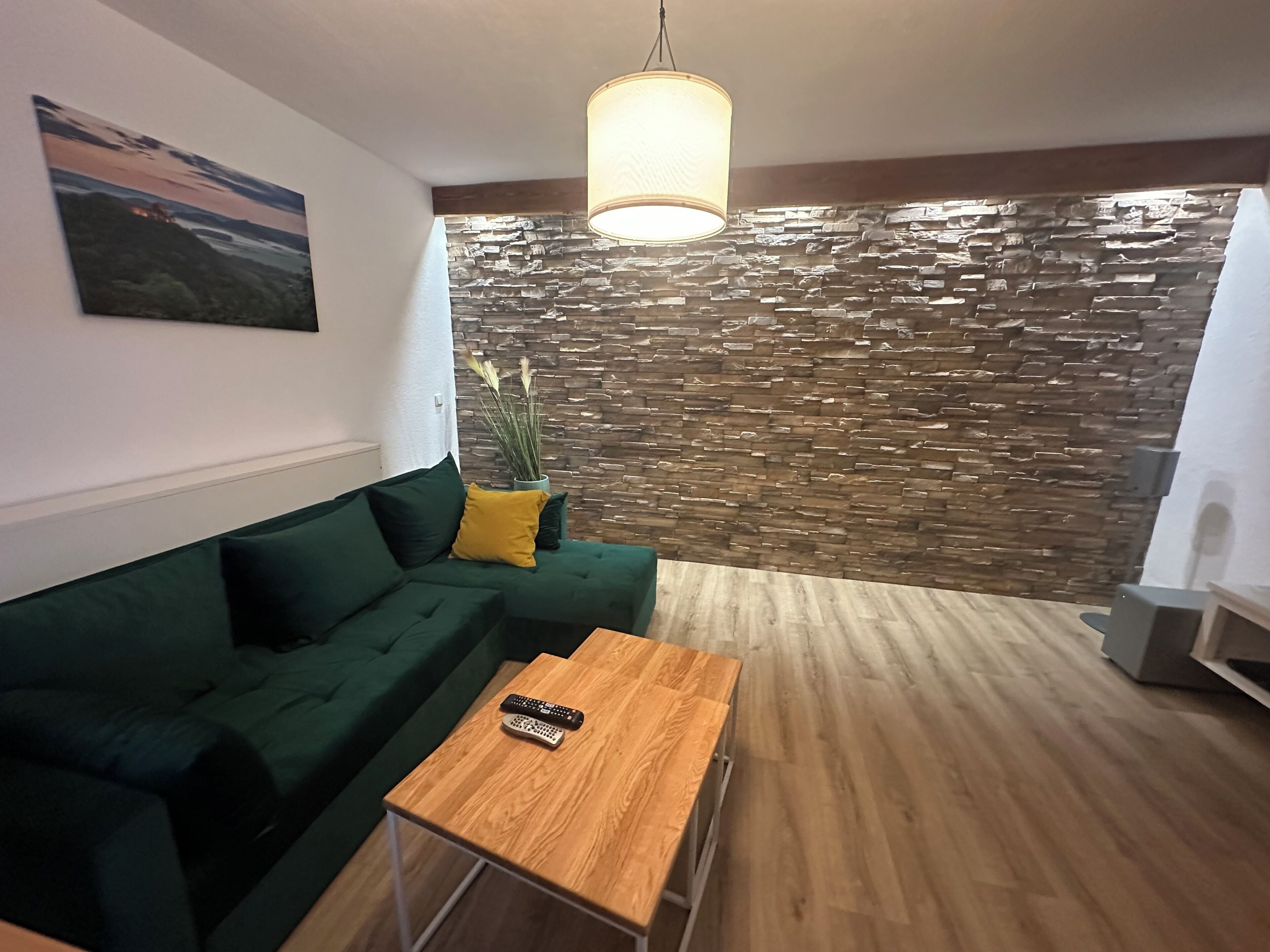 A modern living room with a green sofa, a wooden coffee table, a stone wall, and a hanging light fixture.