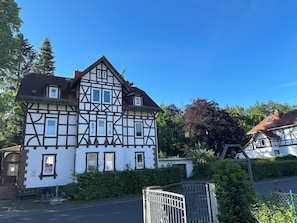 A traditional half-timbered house with a gated entrance, surrounded by greenery.