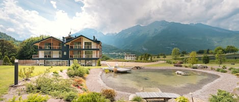 A two-story chalet with a balcony, surrounded by a landscaped garden and a small pond.