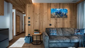 Ein modernes Wohnzimmer mit grauem Sofa, Holzpaneelen, einem runden Beistelltisch mit Pflanze und einem Gemälde.