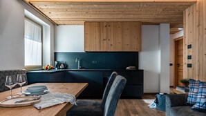 Eine moderne Küche mit Holzausstattung, ein Essbereich mit Tisch für Zwei und ein Sofa im Wohnbereich.