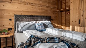 Ein Schlafzimmer mit Holzvertäfelung, einem Bett, Kissen, einer Decke, einem kleinen Tisch mit einer Kamera und einer Pflanze.