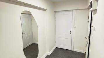 A hallway with a carpeted floor, white walls, and a door with a mirror on the left.