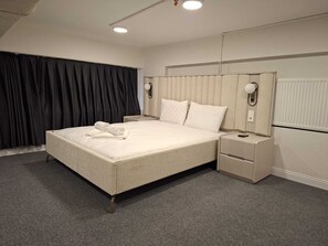 En pænt redt seng med et foldet håndklæde, et natbord med en fjernbetjening og en vægmonteret lampe.