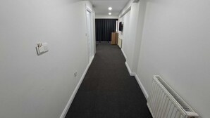 A narrow hallway with white walls, a dark carpet, and a radiator on the right. - Zeynus Hotel Kadıköy (İstanbul)