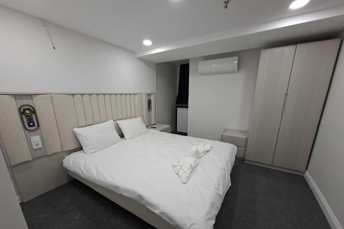Ett modernt hotellrum med en stor säng, ett sängbord, en nattdukslampa, en luftkonditioneringsanläggning och en garderob.