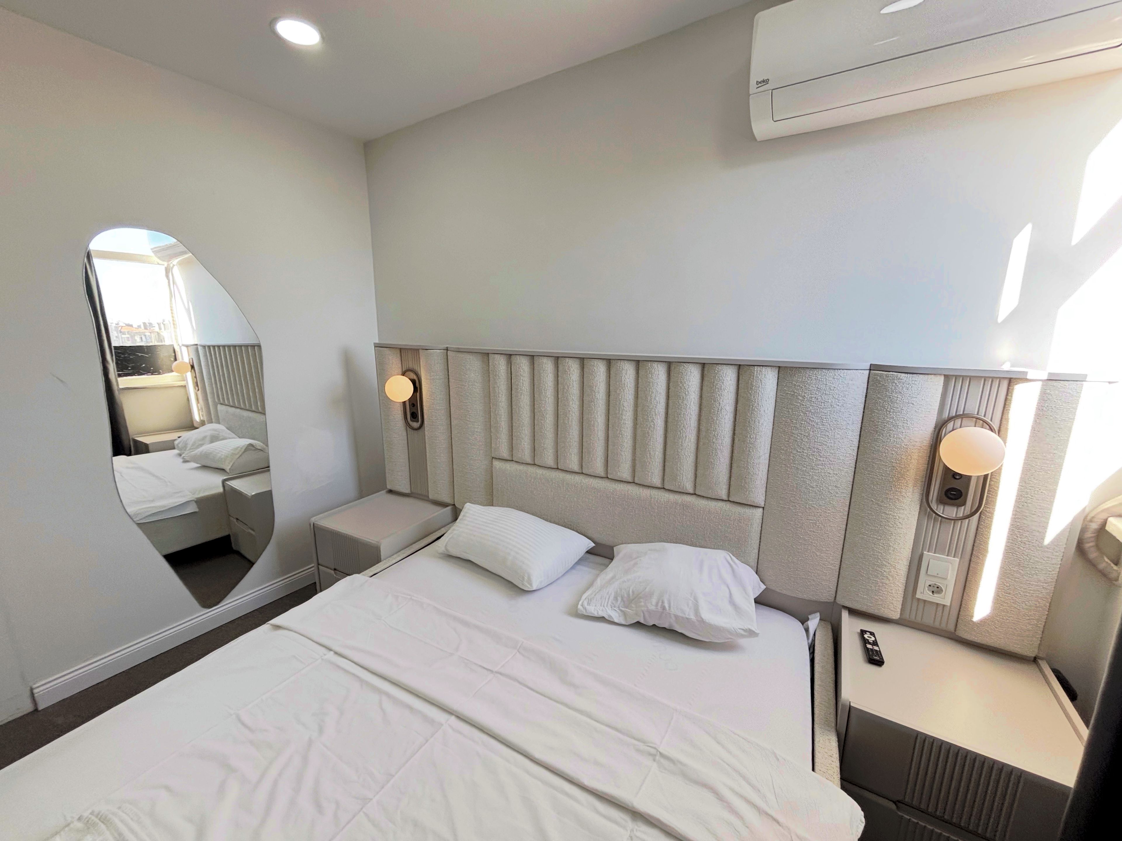 Una habitación de hotel con una cama grande, una mesita de noche, un espejo y un equipo de aire acondicionado instalado en la pared.