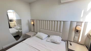 Una habitación de hotel con una cama grande, una mesita de noche, un espejo y un equipo de aire acondicionado instalado en la pared.