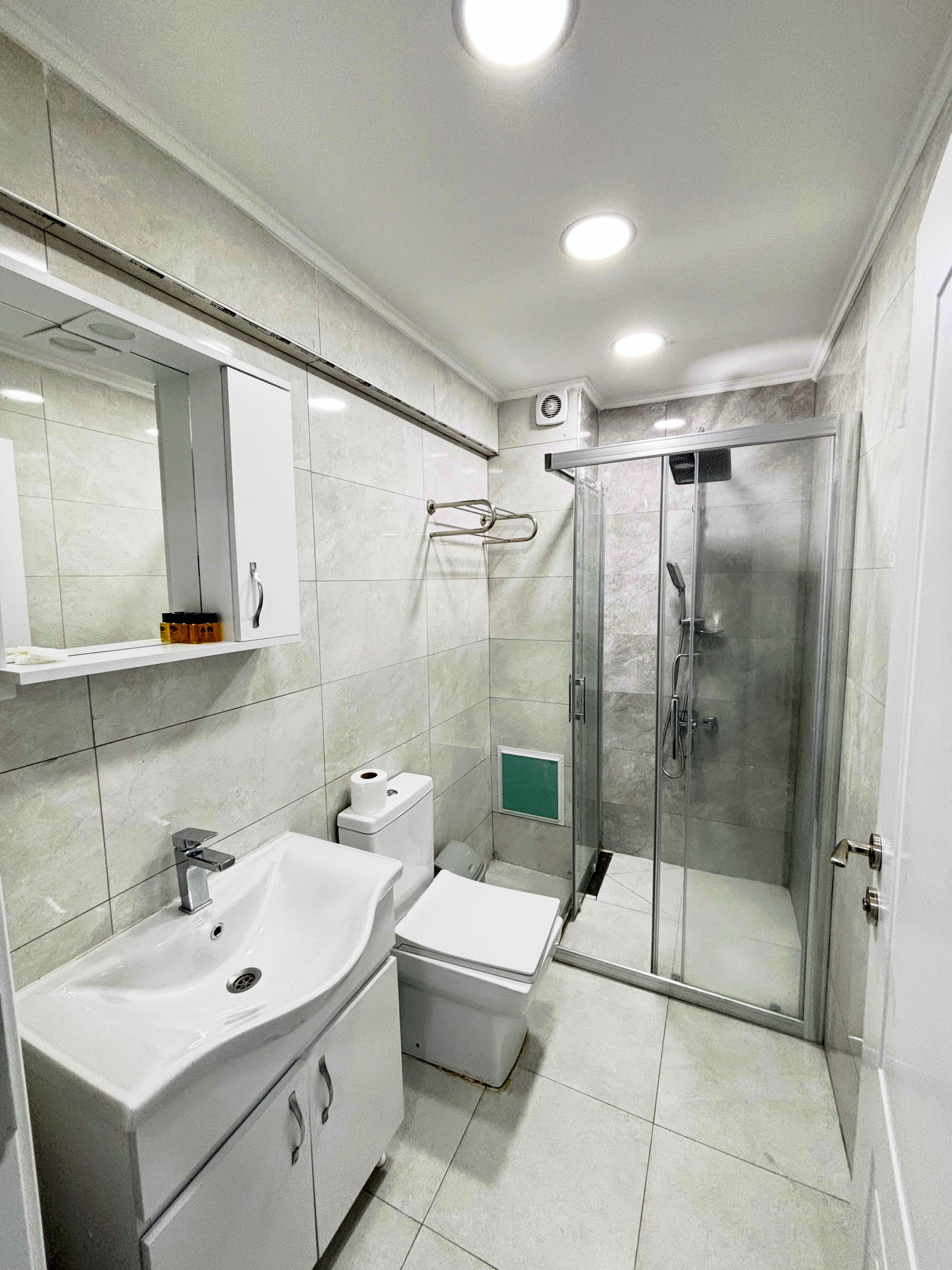 Un baño moderno con cabina de ducha de vidrio, un lavamanos blanco y un inodoro.