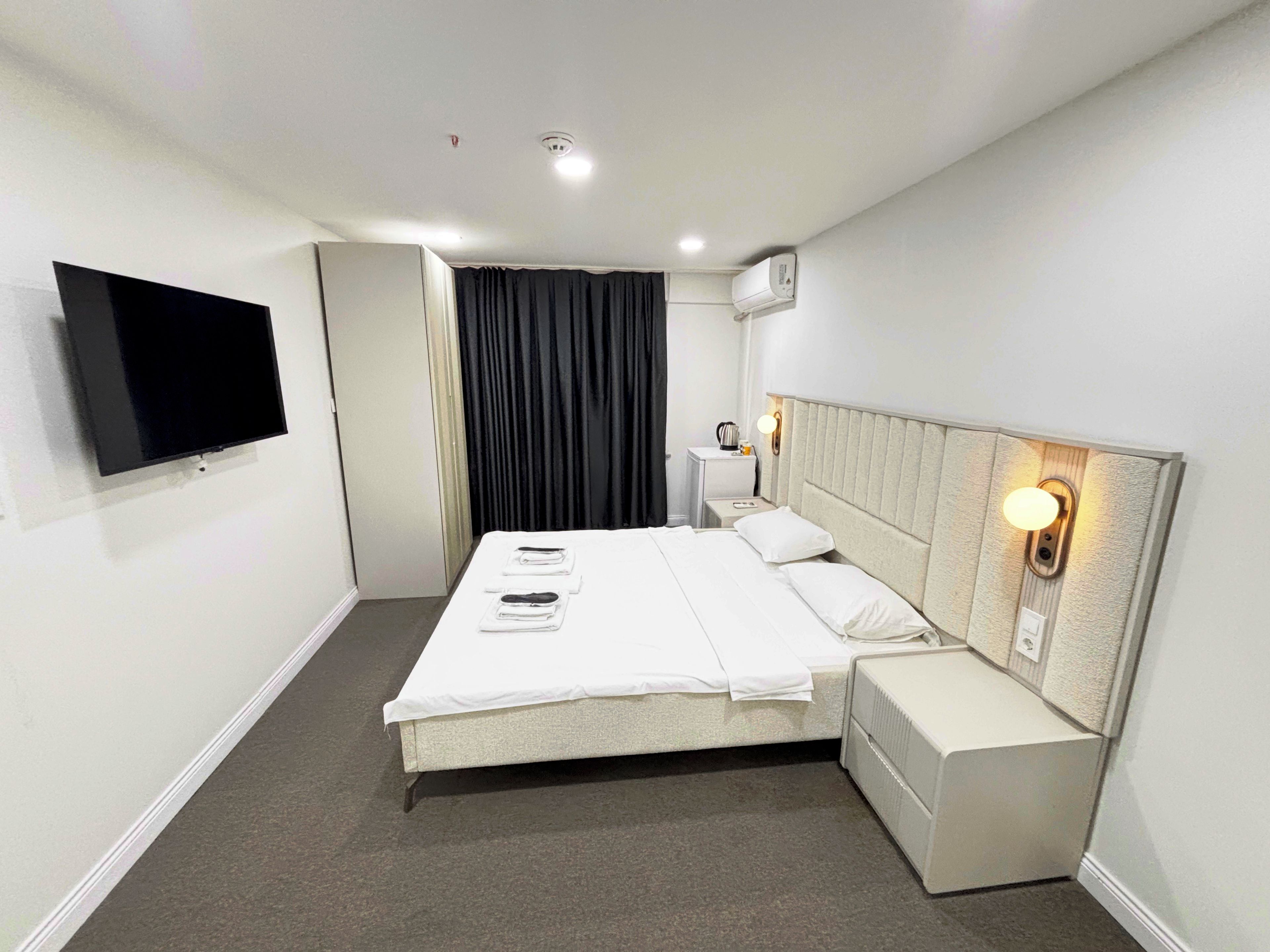 Une chambre d’hôtel équipée d’un lit, d’une table de chevet, d’une lampe et d’un téléviseur fixé au mur.