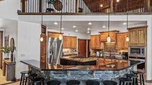 A spacious kitchen with wooden cabinets, a large island with bar stools, stainless steel appliances, and a stone backsplash. - Unwind at Deja View Upper (Hayden Lake)