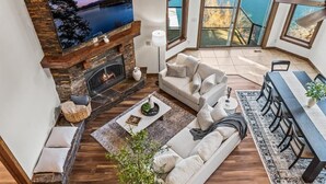 A spacious living area with a stone fireplace, a large flat-screen TV, a sofa, a dining table with chairs, and a view of the outdoors through large sliding glass doors. - Unwind at Deja View Upper (Hayden Lake)
