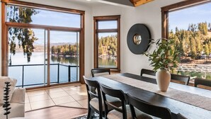 A dining area with a large table, chairs, and a view of a lake and forest. - Unwind at Deja View Upper (Hayden Lake)