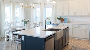 A modern kitchen with a central island, pendant lights, and white cabinetry. - The Sandy Pearl-New showers, golf cart, & fire pit! (Gulf Shores)