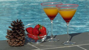 Ein Poolbereich mit zwei Martini-Gläsern, die Schichtgetränke enthalten, einer Erdbeerschale und einer Kiefernzapfen.