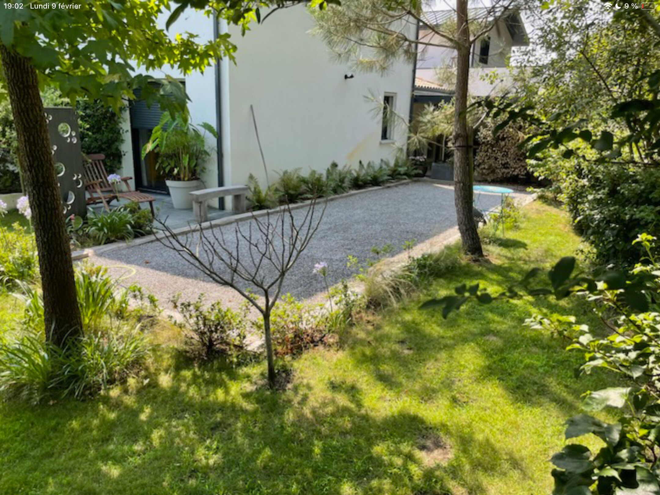 A garden area with a white building, a gravel path, and a bench.