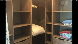 Ein Schlafzimmer mit einem Bett, einem kleinen Hocker und einem Schrank mit Regalen und Schubladen.