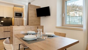Una cocina moderna con microondas, armarios de madera, un televisor montado en la pared y una zona de comedor con una mesa preparada para dos.