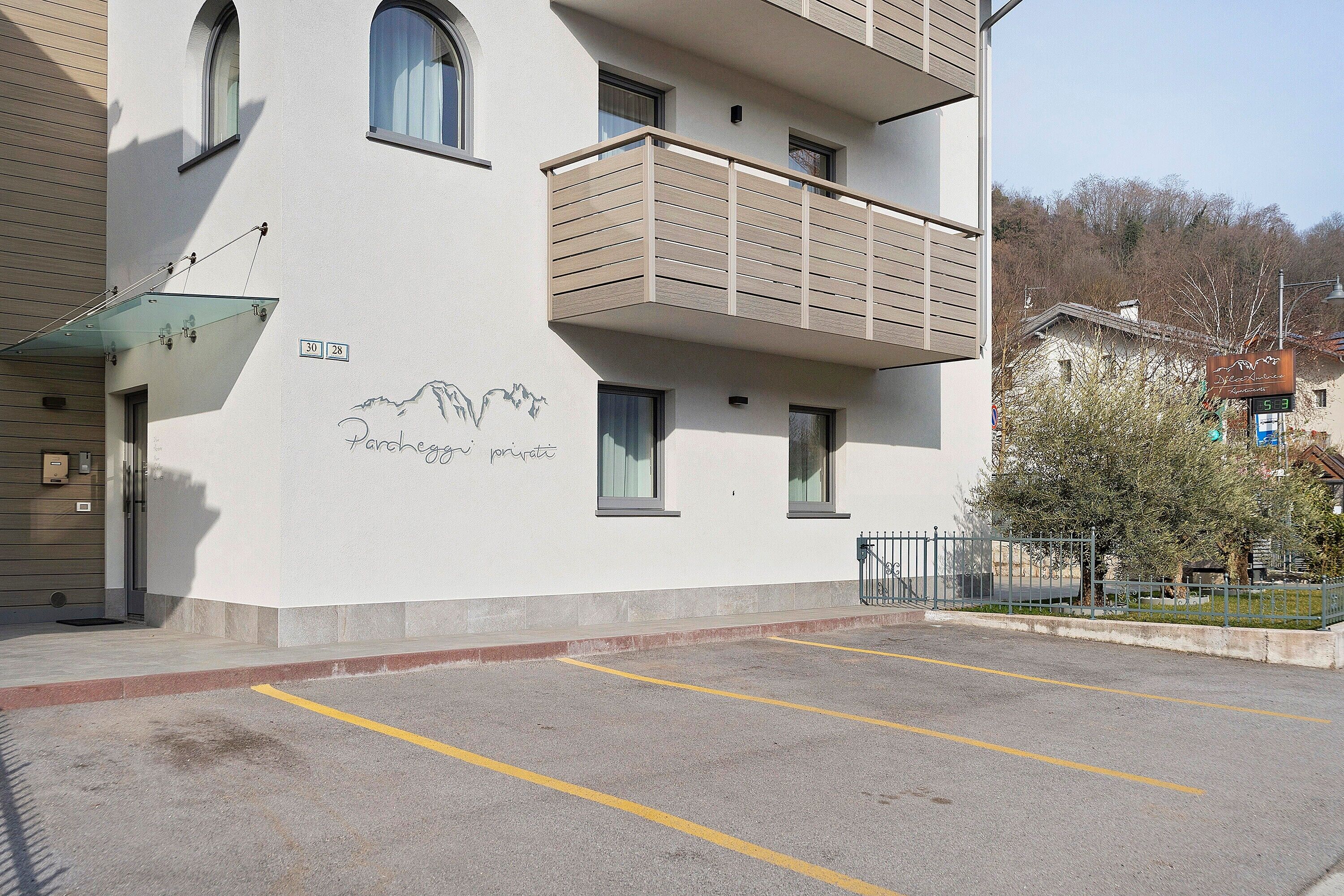 A multi-story building with a balcony, a parking area, and a sign with a mountain graphic.