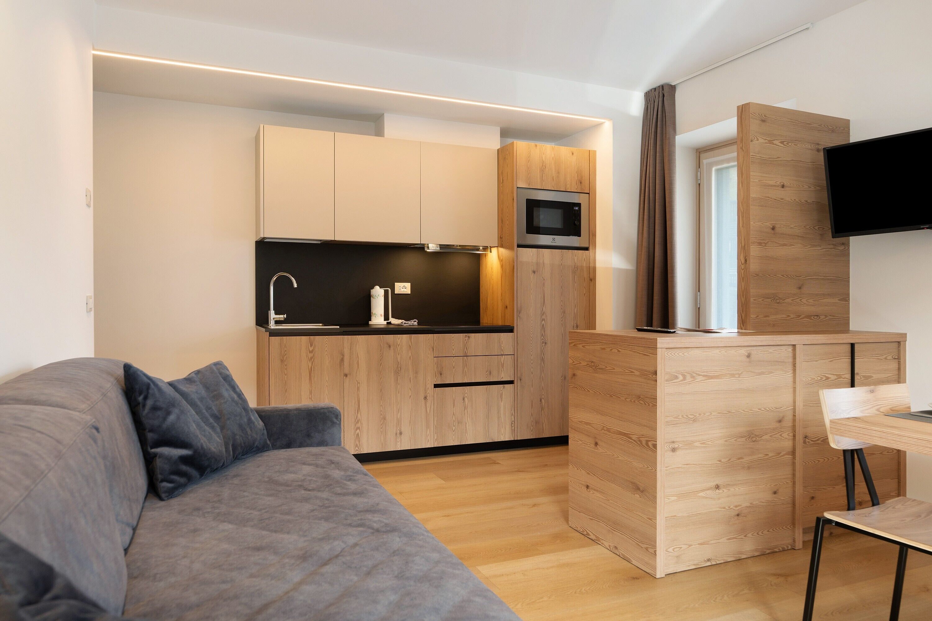 A modern kitchen with wooden cabinets, a built-in microwave, and a flat-screen TV mounted on the wall.